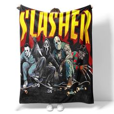 a man is holding up a black blanket with the words slasher on it and two men sitting on skateboards in front of him