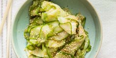 a blue bowl filled with cucumbers and sesame seeds next to chopsticks