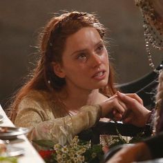 a woman sitting at a table with flowers in front of her and another person standing behind her