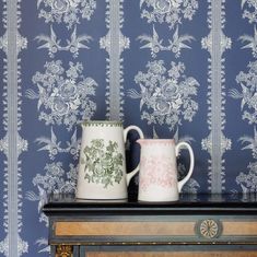 two mugs sitting on top of a table in front of a blue wallpaper