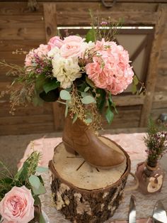 a vase filled with pink and white flowers sitting on top of a tree stump next to silverware