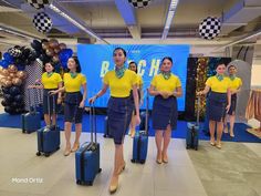 four women in yellow shirts and blue skirts are standing with their luggage at the airport