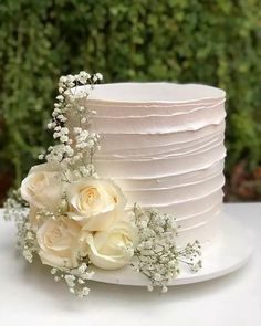 a white wedding cake with flowers on the side and greenery in the back ground