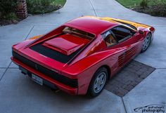 a red sports car parked on the side of a road next to a sidewalk and grass