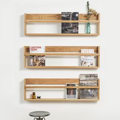 three wooden shelves with magazines and books on them against a white wall behind a stool