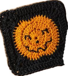 a crocheted black and yellow square with a smiling face on the front side