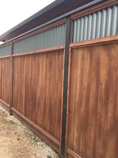 a wooden fence next to a building with metal siding on the top and bottom half