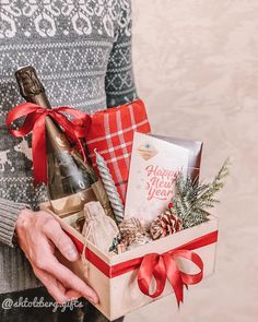 a woman holding a christmas gift box filled with wine, cookies and other holiday treats