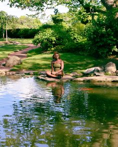 a woman sitting on rocks in the middle of a body of water next to trees