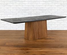 a black marble top dining table on a wooden floor in front of a white brick wall