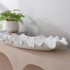 a large white bowl sitting on top of a table next to a potted plant