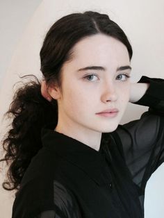 a woman with long hair wearing a black shirt and holding her hand on her head