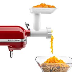 a red food processor and a bowl of cereal on a white background with an orange peel being squeezed into it