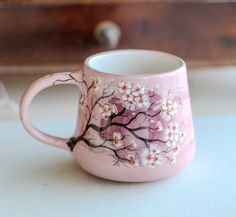 a pink coffee mug with white flowers painted on the outside and inside, sitting on a table