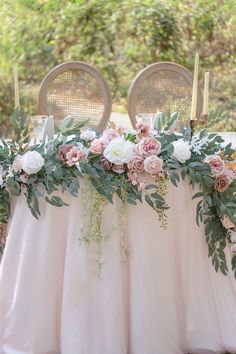 the table is set with pink and white flowers, greenery and candles on it