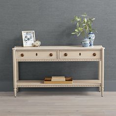 a white table with two drawers and a potted plant on it next to a gray wall