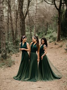 three bridesmaids in dark green dresses standing on a dirt path surrounded by trees