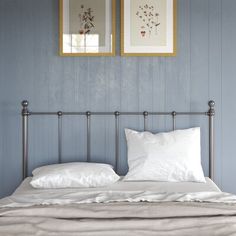 two framed pictures hang above a bed with white linens and pillows on top of it