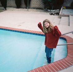 a woman standing in front of a swimming pool with her arms up to the side