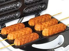 four hot dogs are being cooked in an electric griddle grill with wooden skewers