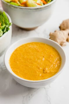 two white bowls filled with yellow soup next to a bowl of salad on a table