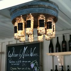 a chandelier made out of wine bottles hanging from the ceiling in front of a chalkboard