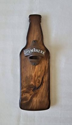 a wooden bottle opener with the words open here on it's side hanging from a wall