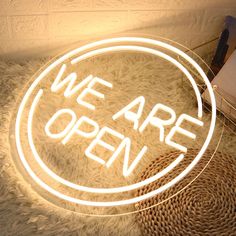 we are open neon sign sitting on top of a white fur covered floor next to a lamp