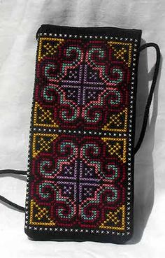 a cross - stitched purse is sitting on a white surface with a black strap