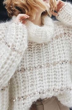 a woman is wearing a white sweater with sequins on the sleeves and shoulders