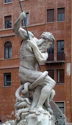 a statue in front of a building with a man holding a stick and sitting on top of it