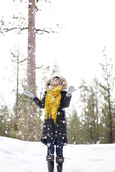 a woman is standing in the snow with her arms out and wearing a yellow scarf