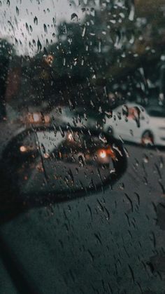 rain drops on the windshield of a car as it drives down a street with other cars