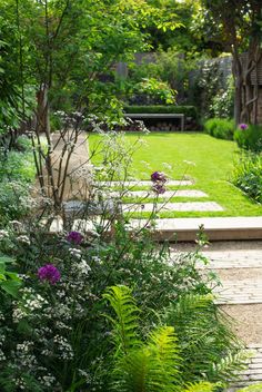 a garden with lots of green grass and flowers on the side of it, next to a stone path