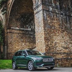 a green volvo suv parked in front of an old brick wall under a bridge with graffiti on it