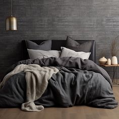 the bed is made up with black linens and grey sheets, along with white pillows