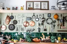 pots and pans are hanging on the wall above a kitchen counter with various cooking utensils