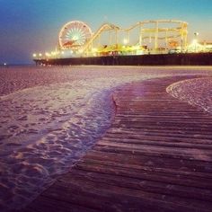 an amusement park at dusk with the boardwalk and ferris wheel in the background