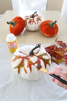 someone is painting a pumpkin with leaves on it and other fall decorations around the table