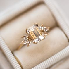 an engagement ring in a white box with gold trimmings and three stone accents