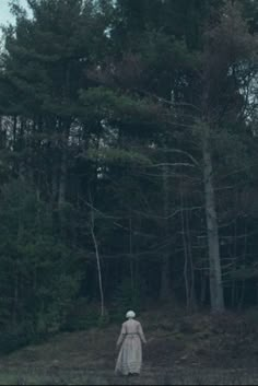 a woman in a white dress is walking through the woods with her back to the camera