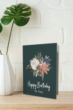 a happy birthday card with flowers in a vase on a table next to a brick wall