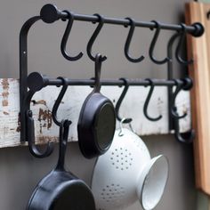 pots and pans are hanging on the wall with black metal racks holding coffee mugs