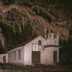 an old white church with moss hanging from it's roof and trees in the background