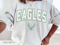 Eagles football collegiate varsity style crewneck sweatshirt Graphic is made using direct to garment printing so you'll never have to worry about cracking or peeling images.  Available in Sand, Military Green, White, Black, & Ash Gray.  Gildan 18000 Unisex crewneck, fits true to size. Size up for an oversized fit.  - Made with a medium-heavy fabric blend of 50% cotton and 50% polyester - Fabric blends: Heather Sport colors - 60% polyester, 40% cotton College Team Spirit Sweatshirt With Lettering, Collegiate Sweatshirt With Letter Print For Fans, Collegiate Style Sweatshirt With Letter Print For Fans, College Varsity Sweatshirt, College Sweatshirt With Text Print For School Spirit, Collegiate Style College Sweatshirt With Lettering, College Sweatshirt With Letter Print For Sports Season, College Sweatshirt With School Spirit Text Print, College Letter Print Sweatshirt For Sports Season