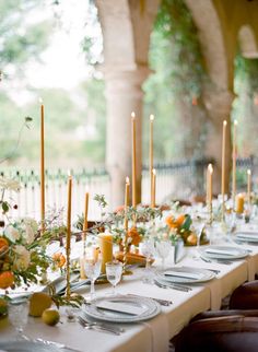 a long table is set with candles and plates for an elegant wedding reception in the garden