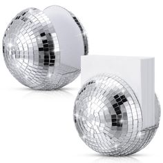 two shiny disco balls sitting next to each other on a white surface and one has a light switch