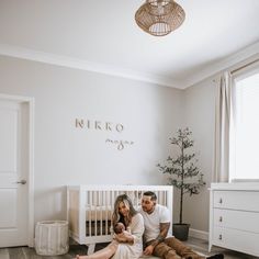 a man and woman sitting on the floor next to a baby crib in a white room