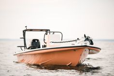 an orange and white boat in the water with a small motorboat on it's side