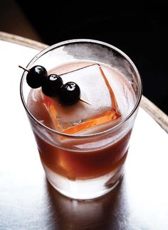 a drink with ice and two cherries on the rim, sitting on a table